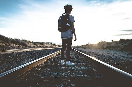 person wearing black backpack standing on railway during daytime