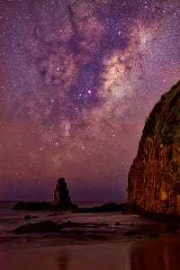 seashore beside mountain under purple and brown sky with stars