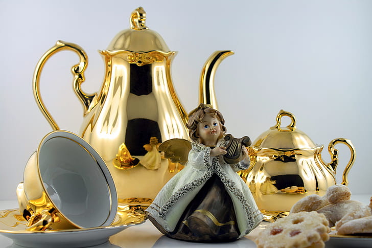angel playing wind instrument figurine beside gold-colored teapots and teacup