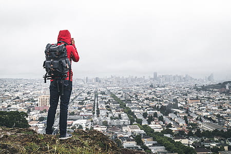 person in red hoodie and black pants with backpack standing at the top of mountain