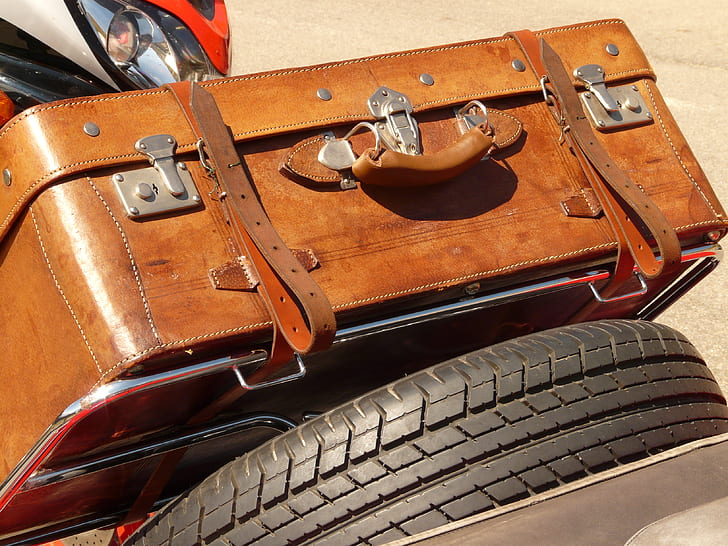 brown leather suitcase beside black auto tire