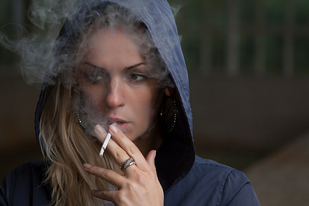 woman wearing blue hooded jacket while puffing a single cigarette