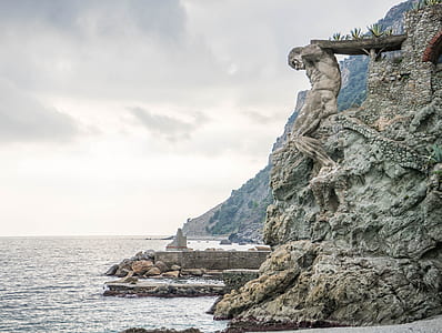 man holding bridge statue on cliff near body of water