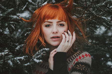 woman with red hair wearing black, gray, and red sweater near tree during snow season