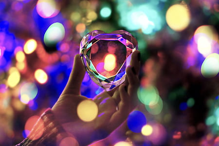 photo of person holding clear heart gemstone with bokeh light background