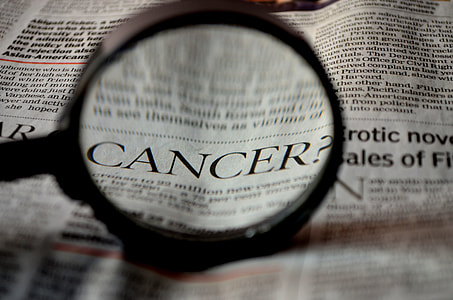 newspaper article with magnifying glass viewing the word of cancer