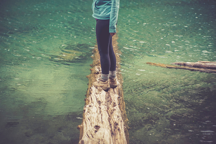 woman in black leggings standing on withered tree log on river