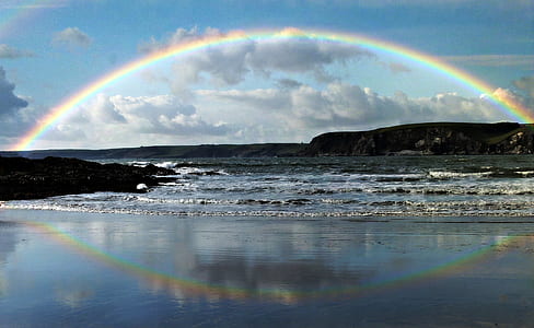 photo of rainbow reflecting on calm body of water