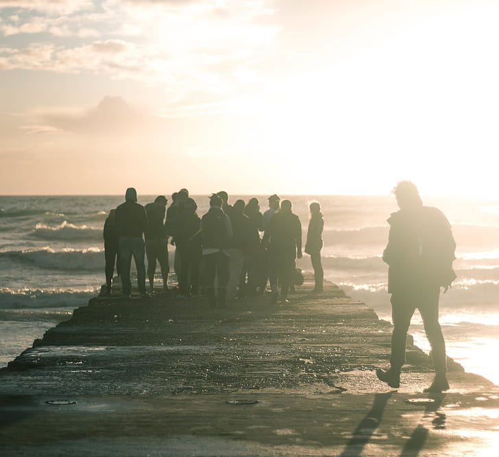 silhouette photo of group of people standing on beach dock
