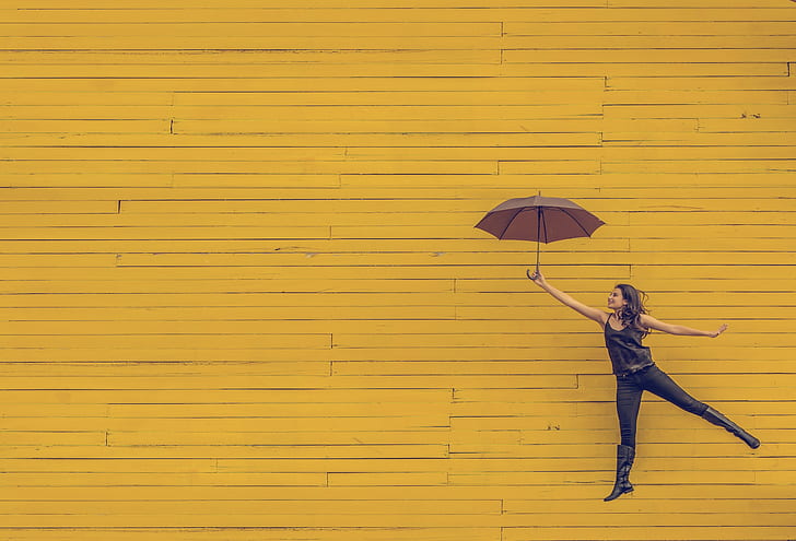 woman holding umbrella jumping on yellow background