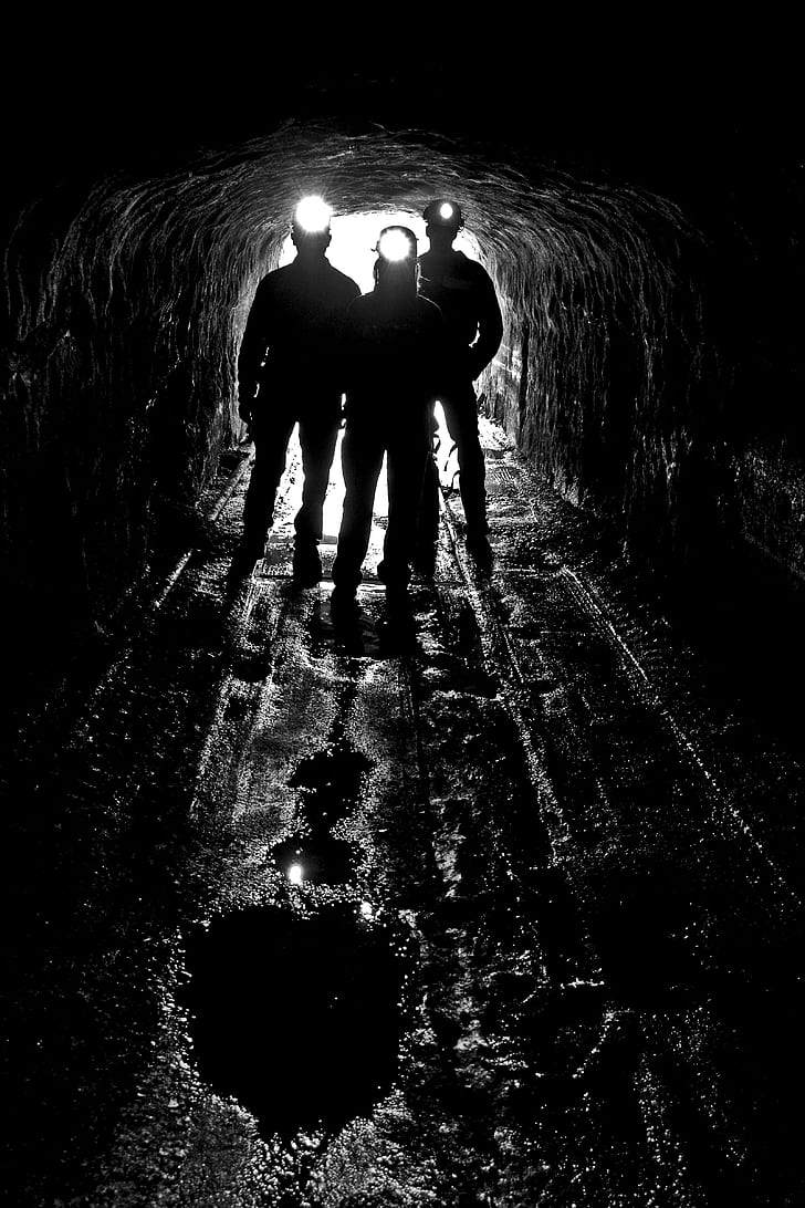 silhouette of three person on cave with headlamp