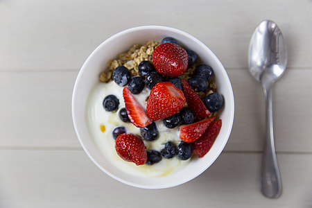 Bowl of yogurt, strawberries, blueberries and granola breakfast cereal with spoon