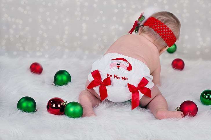 baby in white diaper playing green and maroon baubles
