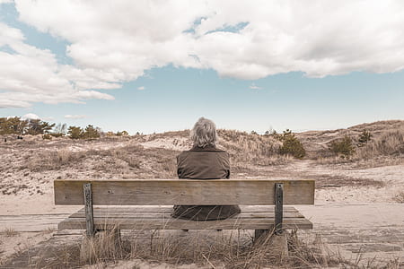 man wearing grey vest sitting on bench under white cloudy sky during daytime