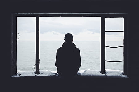silhouette of person sitting on window in front of sea during daytime