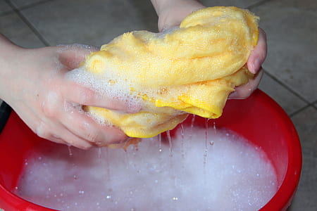 person washing yellow shirt on red plastic basin