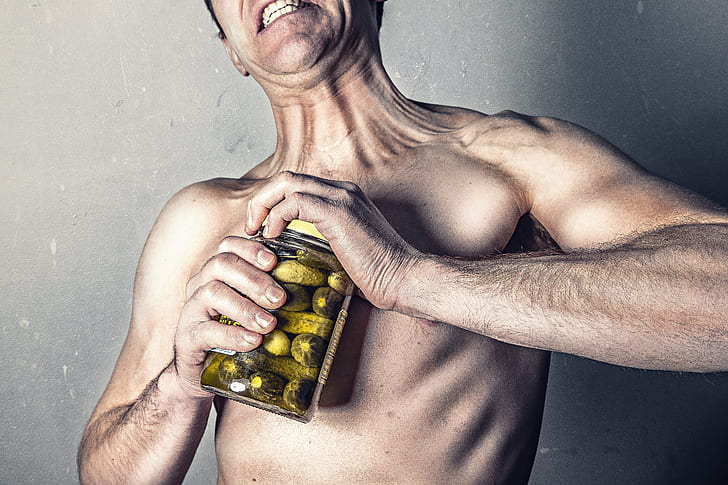 shirtless man opening jar of pickles
