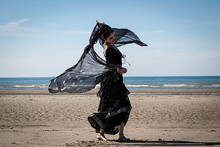 woman in black long dress holding scarf standing on seashore