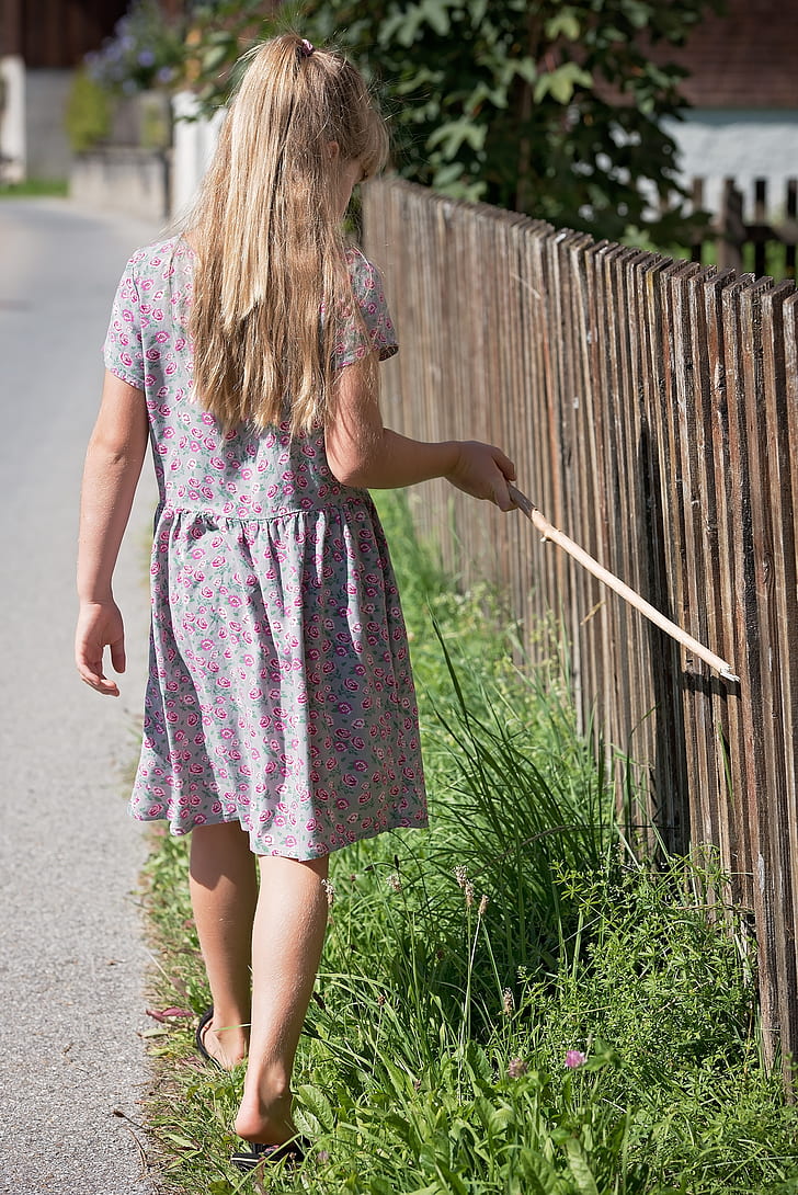 girl holding stick walking beside fence