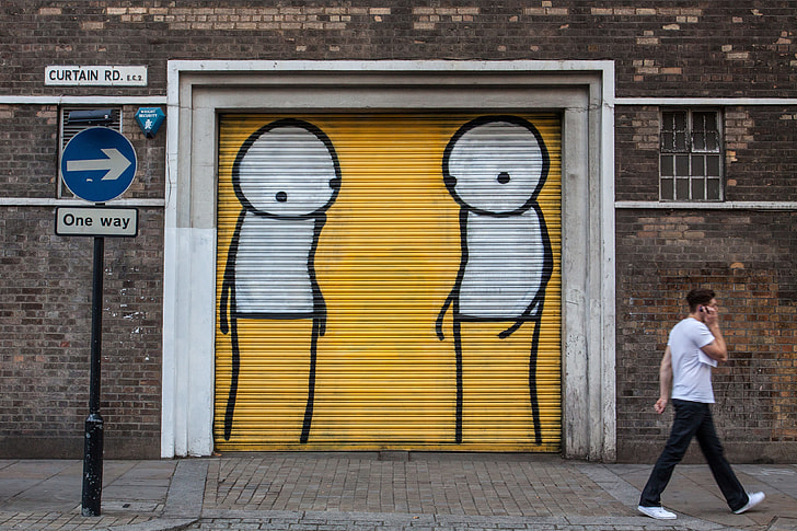 A man walks past a one-way sign and street art background in Shoreditch, East London