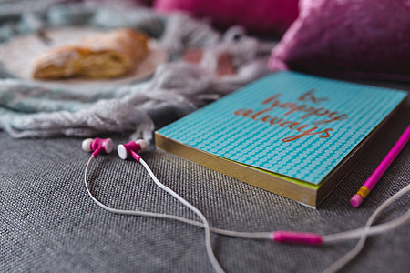 Blue notebook with a pink iPhone, headphones and a sweet bun