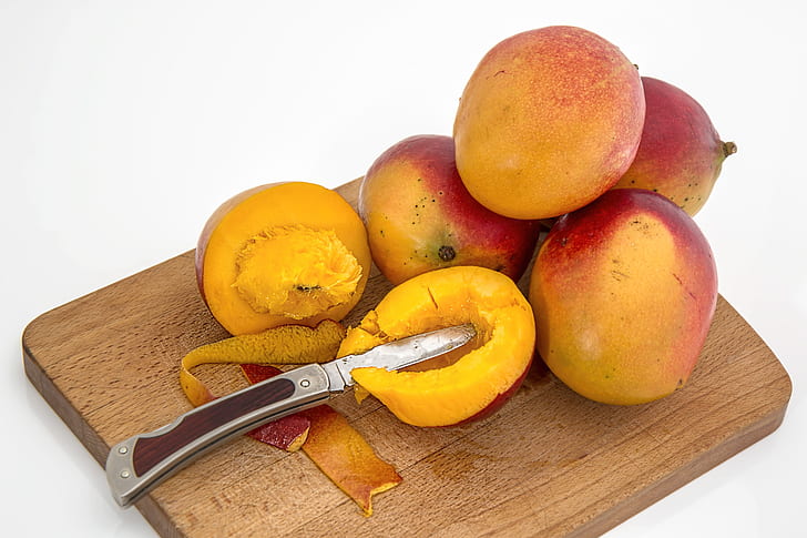sliced mango beside four mangoes on chopping board