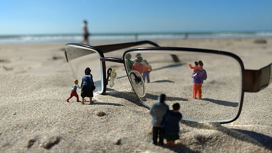 depth of field photography of eyeglasses with people figurines on sand