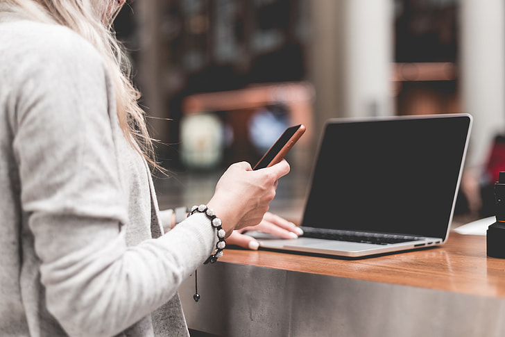 Woman Using Her Smartphone While Working Remotely on Laptop