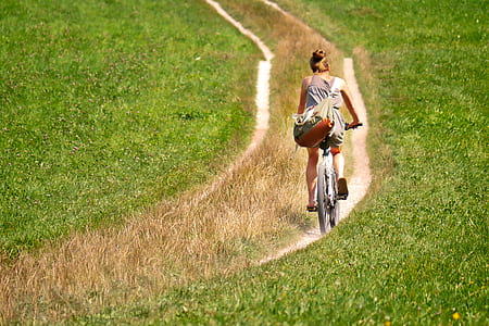 woman with gray tank top riding bicycle on green grass field during daytime