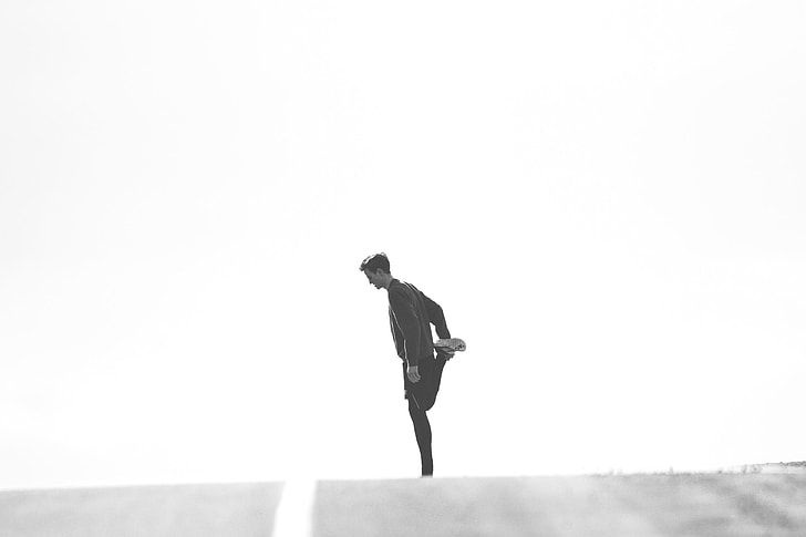man stretching in the middle of road greyscale photo