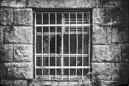 grayscale photo of window grill and wrecked window screen