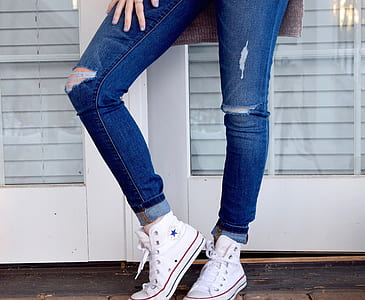 woman wearing distressed whiskered blue jeans and white Converse All-Star high-top sneakers