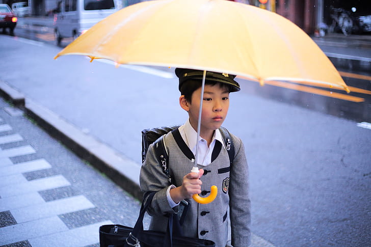 boy wearing school uniform holding a yellow umbrella
