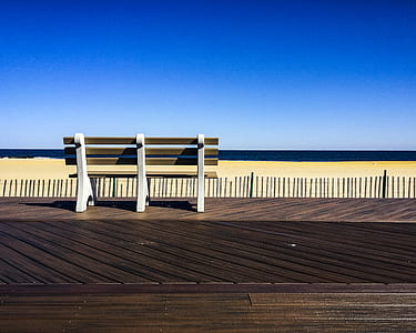 Brown-and-white Wooden Bench Facing Body of Water Under Clear Blue Sky