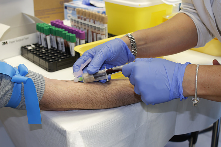 person wearing blue disposable gloves injecting syringe