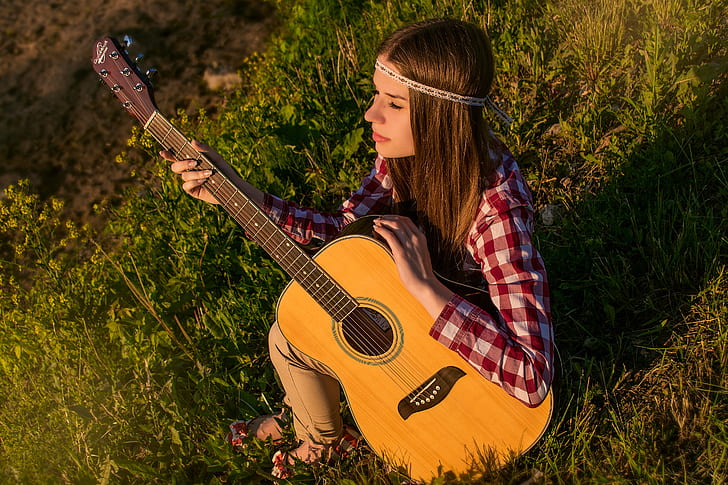 woman in red and white checked sport shirt holding dreadnought brown acoustic guitar