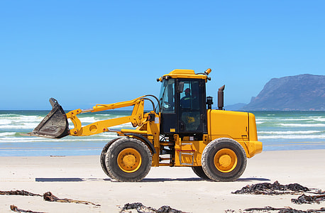 yellow front-end loader on shore near mountain