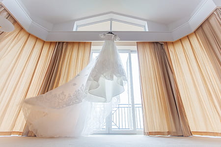 white wedding gown near window curtain