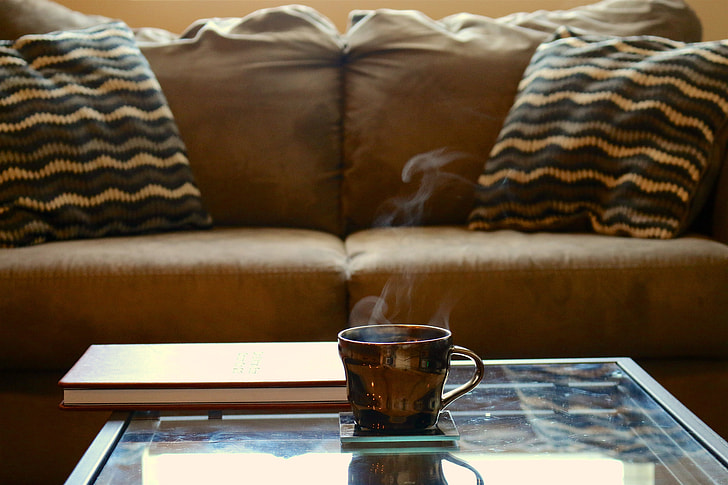 brown ceramic teacup on glass-top coffee table beside brown sofa