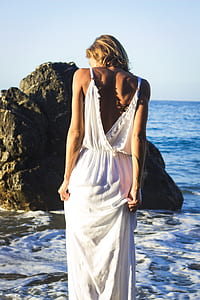 woman wearing white dress facing the sea with rock formation