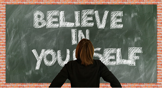 person in black long-sleeved top facing blackboard with believe in yourself text
