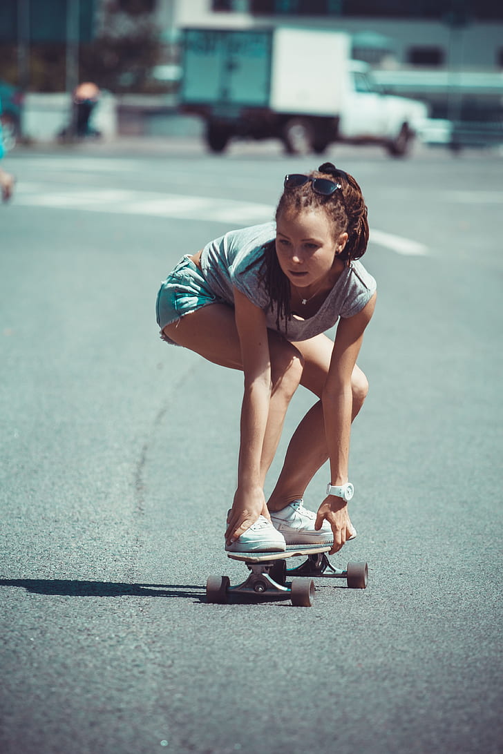 girl in white shirt and teal shorts riding skateboard at daytime
