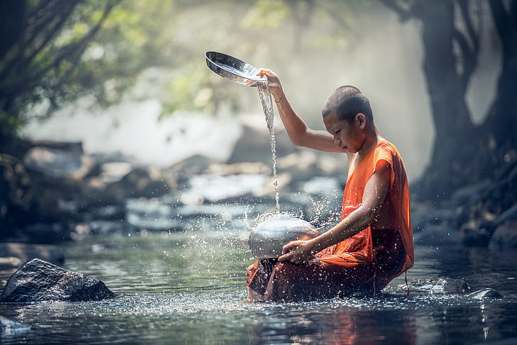 shallow focus photography of monk pouring water on silver pot at river