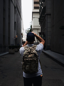 man wearing cap and backpack standing between buildings