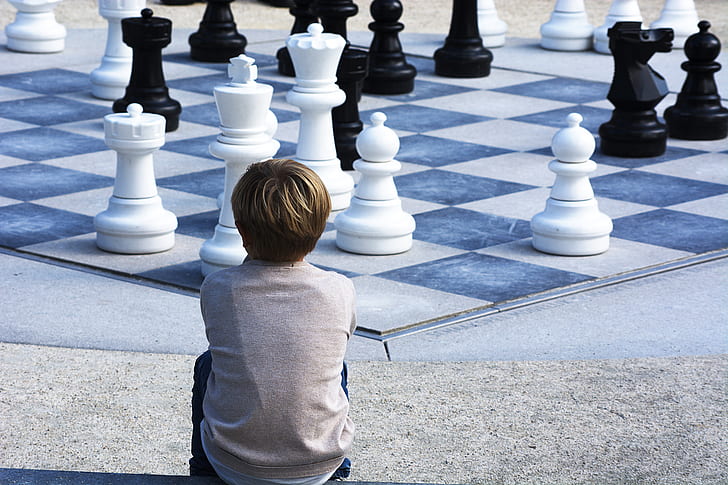 boy sitting watching white and black giant chess board
