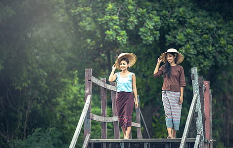 two women with hat walking on gray wooden bridge during daytime
