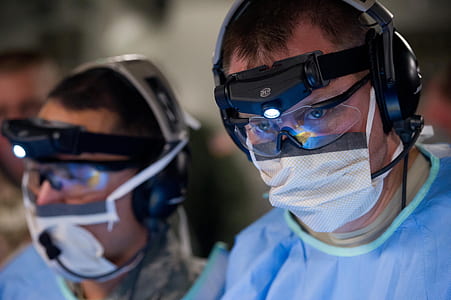 two men in blue lab gowns, face masks, and black-framed 3D glasses