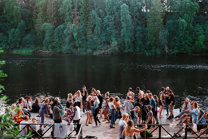 people gathered near lake surrounded by green trees