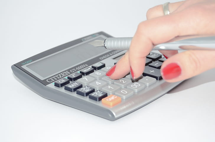 person pressing button on desk calculator