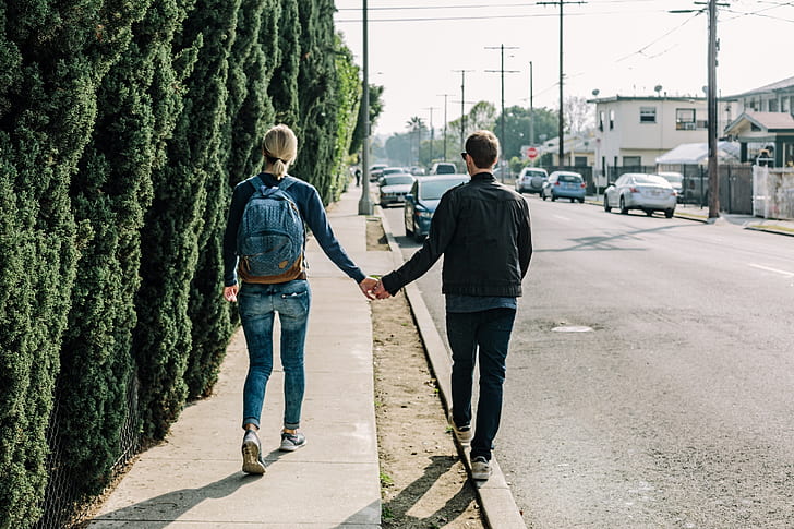 woman and man walking on sidewalk while holding hands